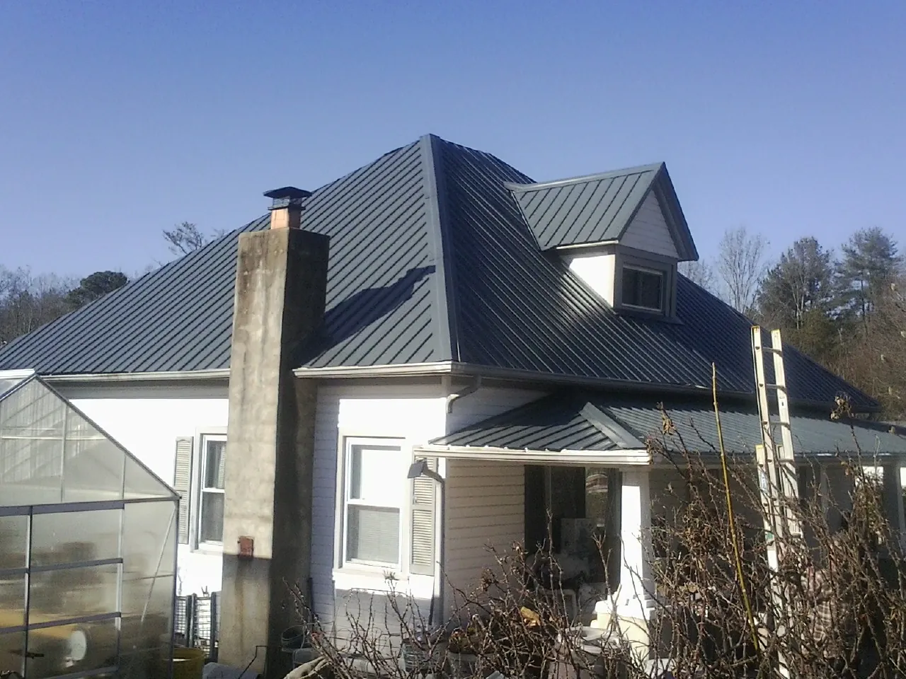 Dark blue standing seam metal roof on a white farmhouse with dormer — Slate & Tile Roof Repair by Roofing Brothers in New Derry