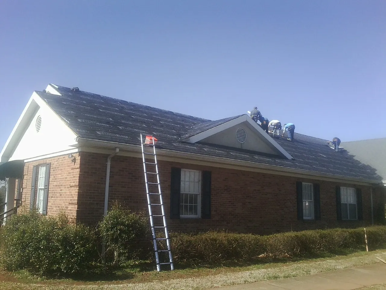 Crew tearing shingles off a brick ranch roof with a ladder set — Emergency Roof Repair work by our crew in New Derry