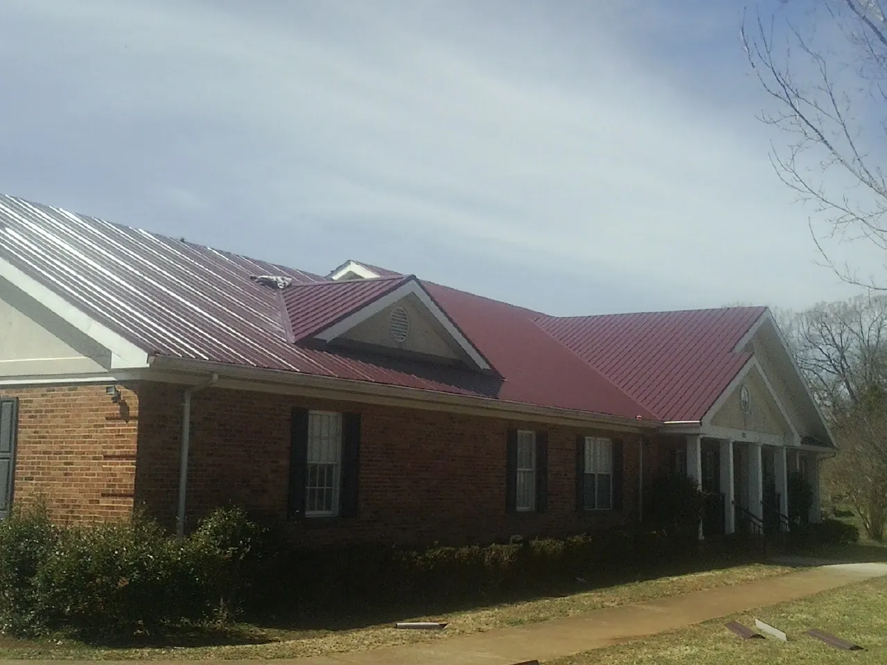 Red metal roof with gabled entries on a long brick building, from a Hail Damage Roof Repair job in New Derry