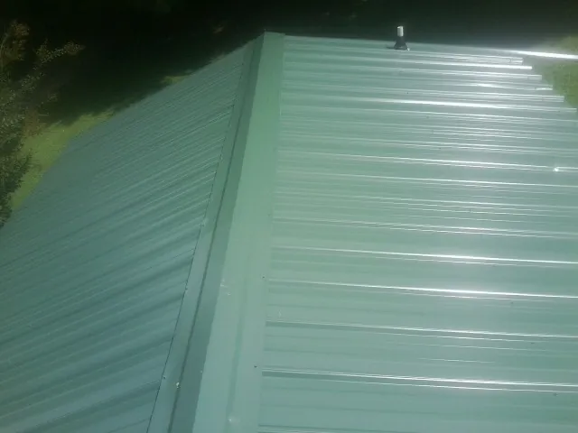 New green metal panels meeting at the ridge of a roof — Flat Roof Repair work by our crew in New Derry