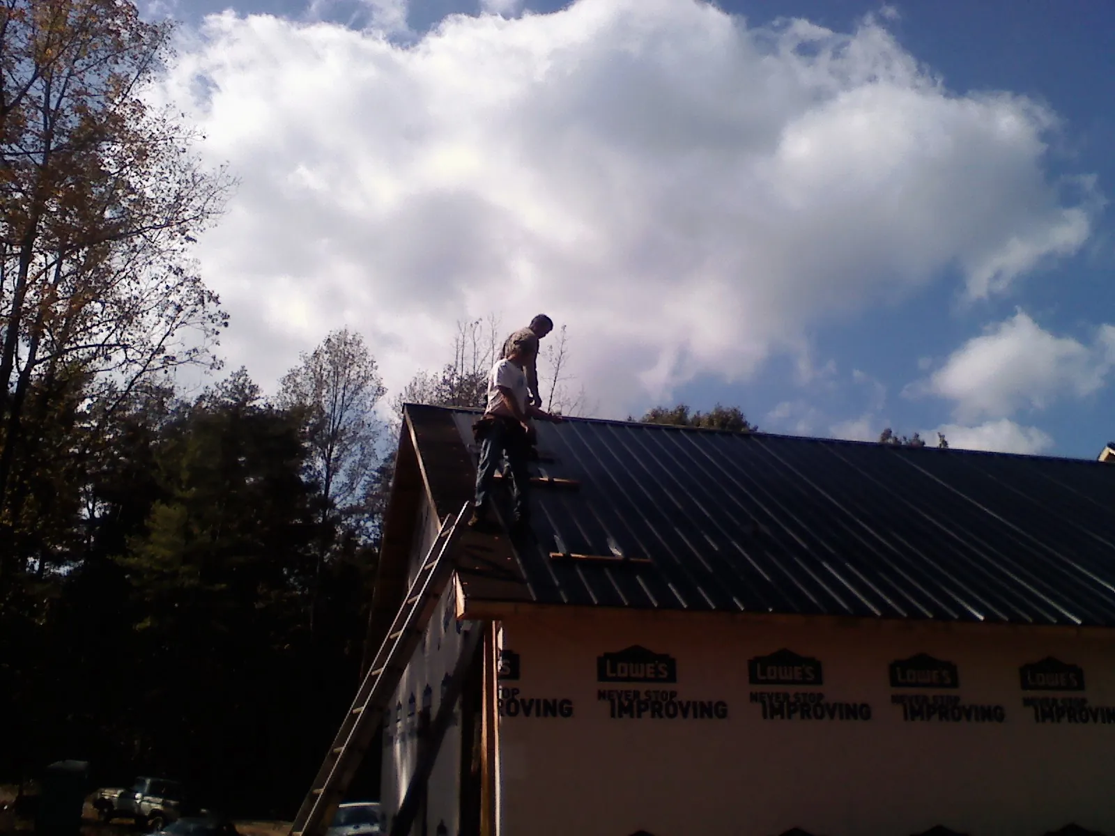 Roofer fastening dark metal panels high against a cloudy sky, from a Roof Inspection job in New Derry