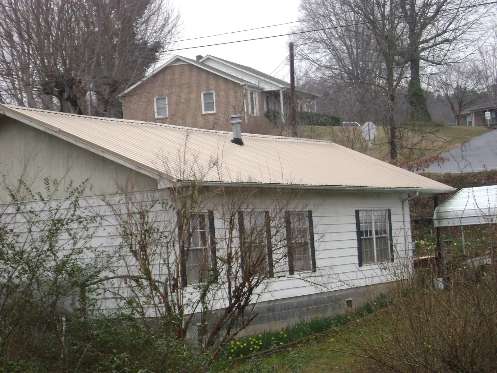 Tan metal roof on a white sided house set into a hillside — Commercial Roofing by Roofing Brothers in New Derry